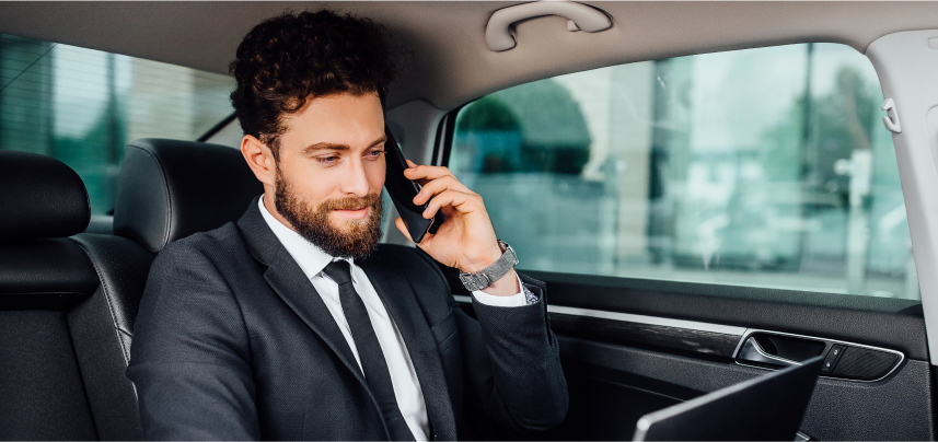 A business professional on a call and using a laptop in the back of a car, representing corporate car for rent in Islamabad and Rawalpindi from Micro Car Rental.