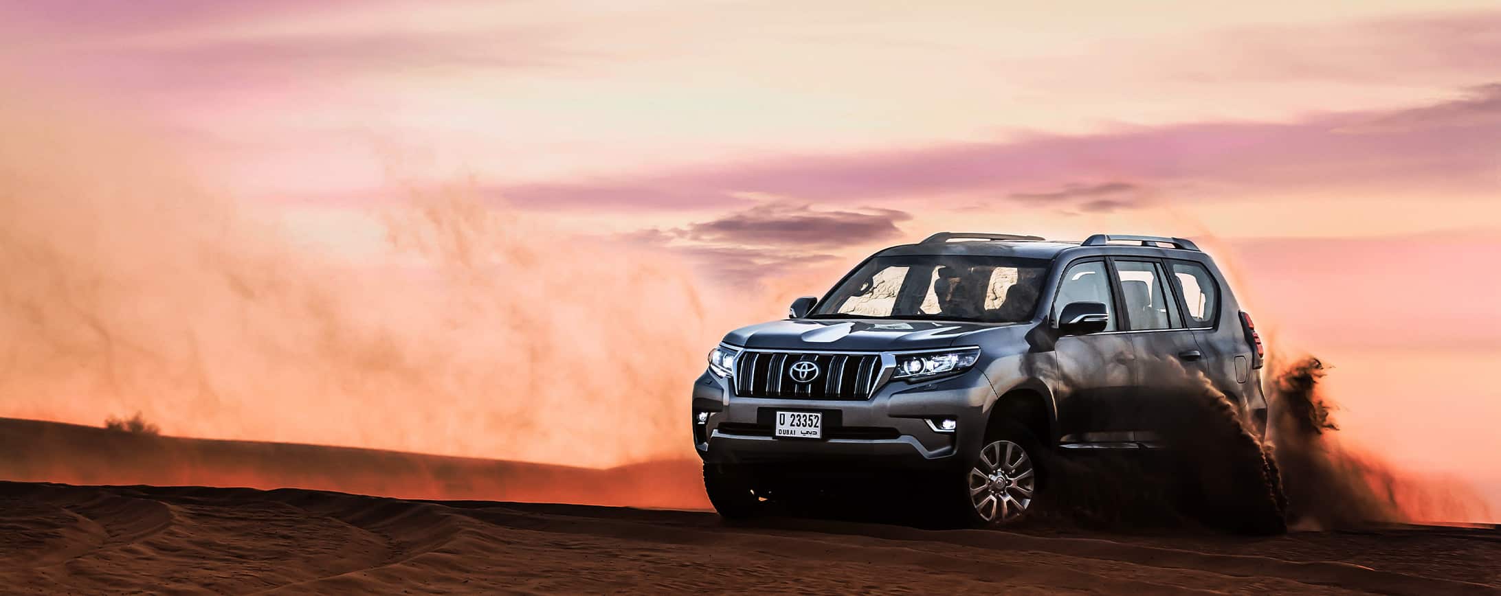 Image of a dark gray Toyota Prado for rent, kicking up dust on an adventure drive, from Micro Car Rental in Islamabad.